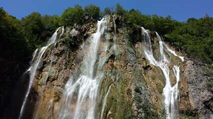Obraz premium Waterfalls in Plitvica park, water falling from top of the hill with trees on top of it. 