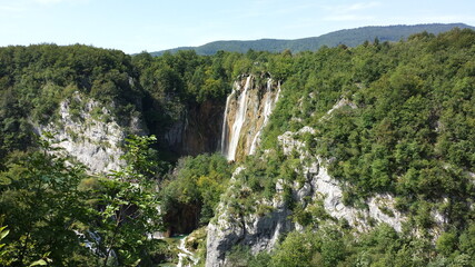 Nature with waterfall in Plitvice National Park, waterfall in the middle surrunded with trees and bushes. Water falling from top of the hill down to a small lake.