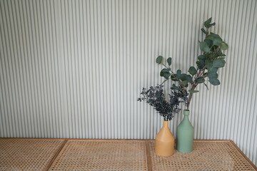 Nice artificial plant in ceramic vases setting on empty rattan bench with white corrugated wall in minimal modern style apartment / residential interior concept / copy space