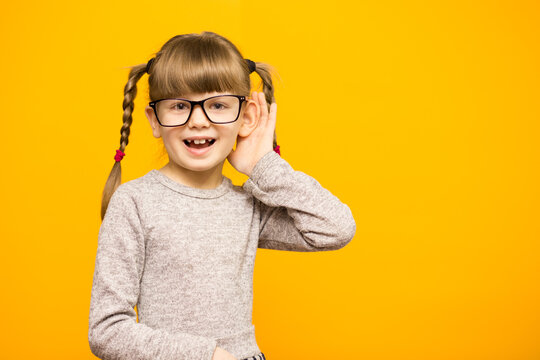 Little Child Girl Journalist In Glasses With Surprised Euphoria Face And Funny Pigtails Listening To Something Holding His Hand To Ear