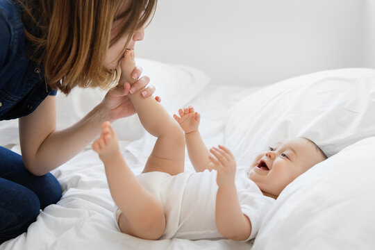 Young mother playing with baby feet on bed