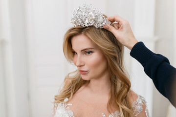 Bride in a magnificent wedding dress posing in a light interior photo studio. Vintage design. Straightens the tiara with his hand © Denys
