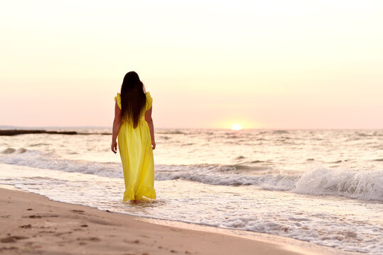 A beautiful XL-size girl with long black hair and a yellow long dress walks along the seashore in the early morning at dawn. beautiful idealistic landscape of sea rest and relaxation.