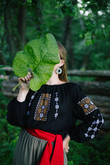 Girl in embroidered shirt with big leaf of burdock holding in front of her face. For design....