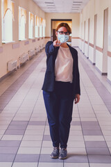 Fototapeta premium Female teacher in face mask stands in an empty school corridor. Coronavirus quarantine concept