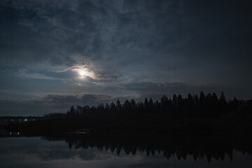 Blue sky on sunset, reflected in a pond water, with sun rays beaming from behind clouds