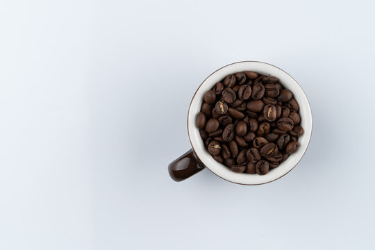 Specialty java coffee, dark roast, a cup filled with coffee beans top view on white background, text space