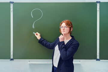 School teacher stands at the blackboard with a chalk drawn question mark. The female teacher stands...