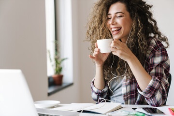 Photo of cheerful young woman drinking tea while working with laptop