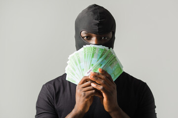 young african man in a black robber mask, and in a black t-shirt on a gray background with euro in...