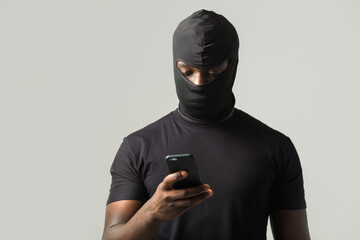 African man in a black robber mask, and in a black T-shirt on a gray background with a mobile phone...