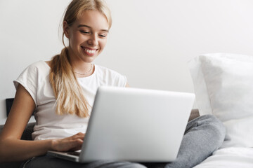 Photo of woman smiling and working with laptop while sitting on bed