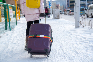 Young woman carrying luggage on the footpath in the winter.