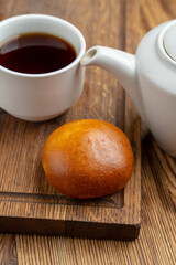 Single russian stuffed pirozhok with black tea on wooden table
