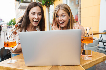 Image of delighted women expressing surprise while using laptop