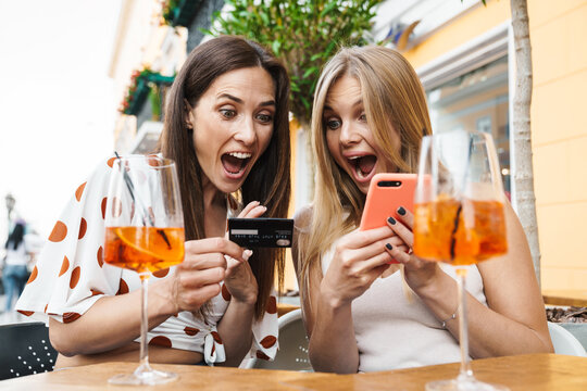 Image of women holding card and cellphone while drinking cocktails