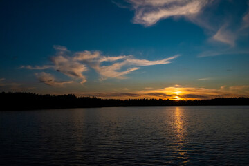 Naklejka premium Panorama of a gorgeous sunset at a forest lake, with gold and blue color in the sky and trees reflected in the water. High quality photo