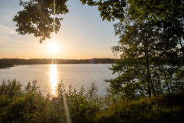Fototapeta premium Panorama of a gorgeous sunset at a forest lake, with gold and blue color in the sky and trees reflected in the water. High quality photo