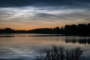 Fototapeta premium night landscape with white silver clouds over the lake, blurred foreground, charming cloud reflections in the lake water, summer night