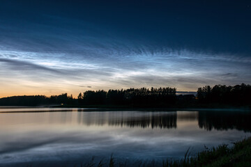 night landscape with white silver clouds over the lake, blurred foreground, charming cloud reflections in the lake water, summer night