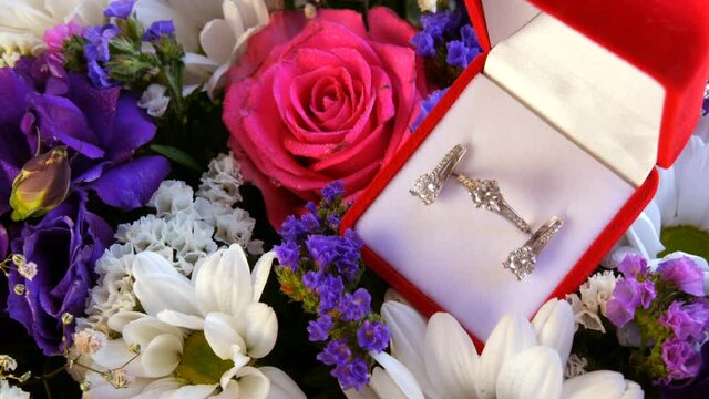 Gift present red box with a set of engagement ring and earrings on the background of a multi-colored beautiful bouquet of flowers. Marriage proposal. White gold or silver with diamond stone