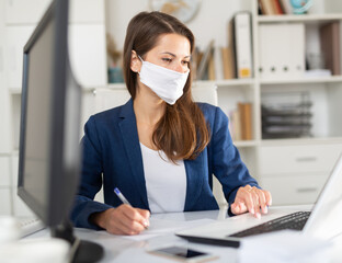 Portrait of confident woman wearing medical mask working on laptop in office. New life reality...