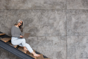 Obraz premium Mature woman sitting on steps using laptop computer.