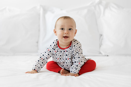 Cute baby girl sitting on white bed looking away