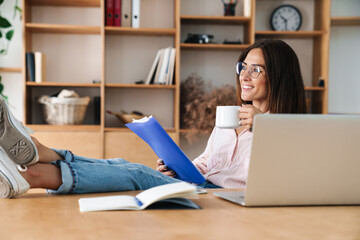 Image of smiling businesswoman drinking coffee and reading documents