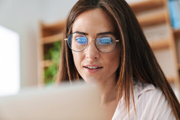 Image of focused adult businesswoman in eyeglasses working with laptop