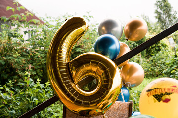 Composition of helium balloons gold and blue - large figure of six in gold color outside - blurred background