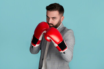 Serious young businessman in boxing gloves ready to fight against blue background