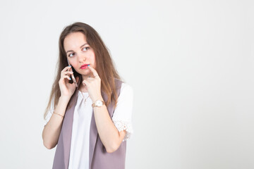 beautiful young woman in business strict clothes poses against a white wall with a phone in her hands