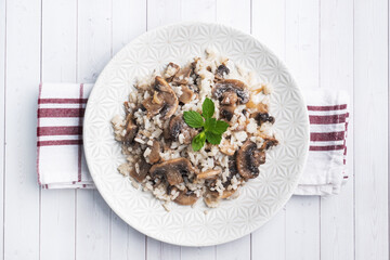 Risotto with mushrooms on a white plate. Boiled white rice with champignons in cream sauce. Light wooden background. Copy space