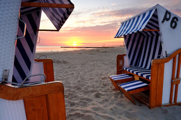 Wschód słońca na wybrzeżu Morza Bałtyckiego,kosze plażowe stoją na piaszczystej plaży w Kołobrzegu,Polska. - obrazy, fototapety, plakaty