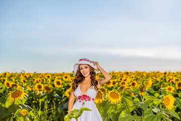 Beautiful woman poses in the agricultural field with sunflower on a sunny summer day