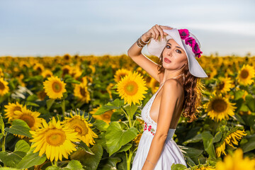 Beautiful woman poses in the agricultural field with sunflower on a sunny summer day