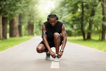 Black sportsman tying shoelaces at park jogging path