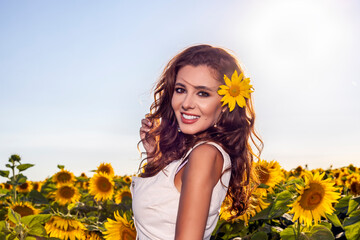 Beautiful woman poses in the agricultural field with sunflower o