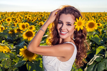 Beautiful woman poses in the agricultural field with sunflower on a sunny summer day