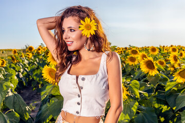 Beautiful woman poses in the agricultural field with sunflower on a sunny summer day