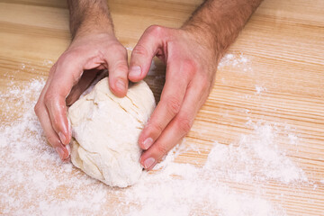 Man's hands working with dough on the wooden table