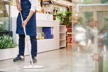 Waiter in apron wiping floor in cafe in the morning before opening - obrazy, fototapety, plakaty