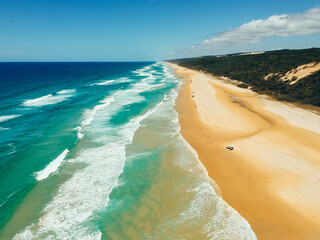 Cars driving along 75 Mile Beach on Fraser Island amongst massive waves