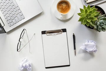 Clipboard mock-up on the table with coffee, glasses, laptop and crumpled paper