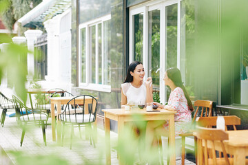 Fototapeta premium Beautiful young Vietnamese women enjoying tasty breakfast in outdoor cafe