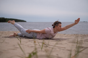 Woman doing yoga shalabhasana or locust pose on the beach