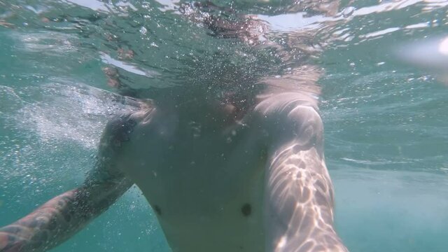 Underwater view of Happy active man using action camera to film himself at the beach. Diving and swiming