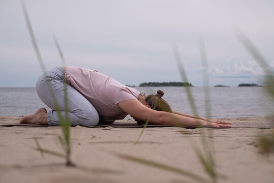 Sporty young woman practicing yoga, sitting in Child exercise, Balasana pose, working out. Outdoor full length on beach
