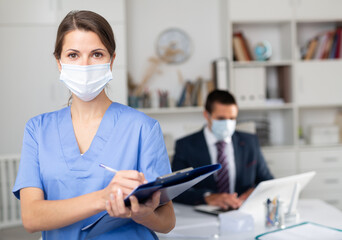 Female medical worker in protective face mask meeting staff in office. Concept of monitoring health...